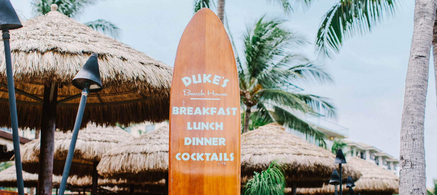 Surfboard menu with main course names in tropical area with cabanas