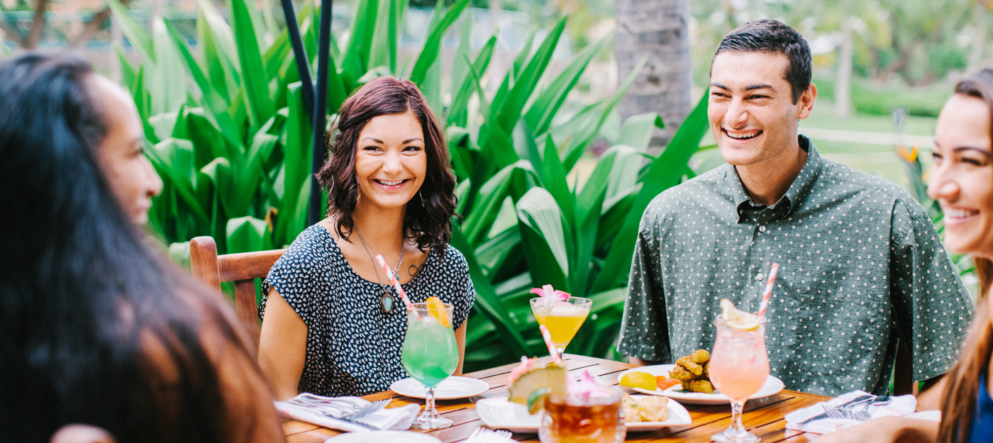 Four people smiling at a table with drinks and appetizers