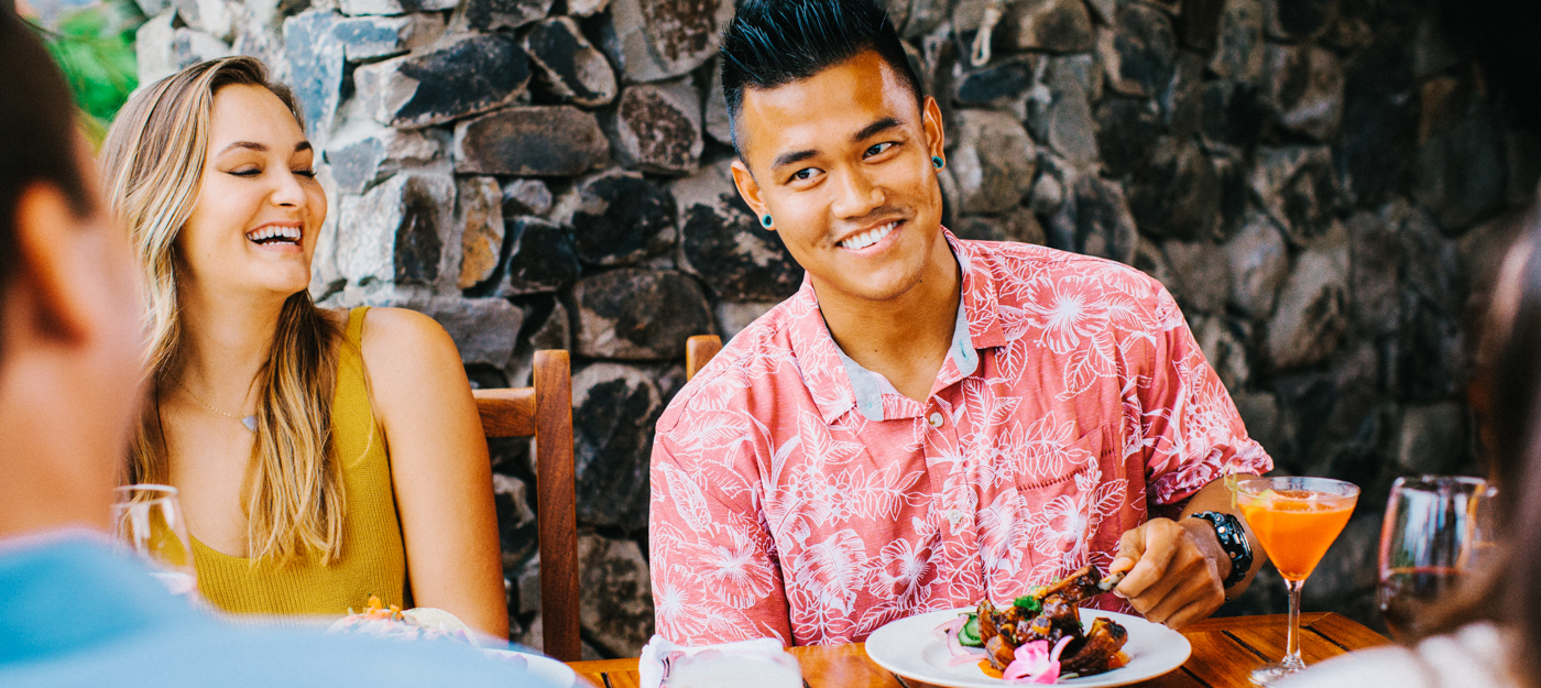 A man smiling while eating ribs at the table with two friends