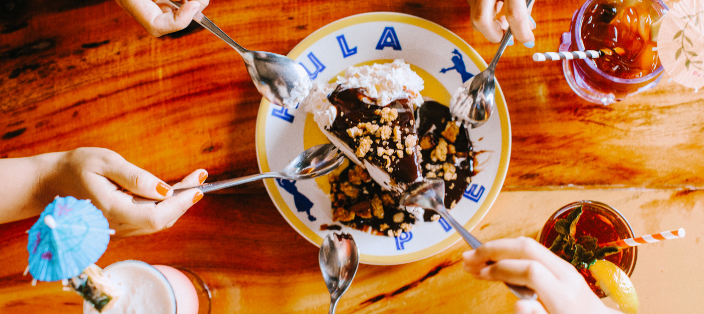 Five people sharing a slice of cake with fudge and whipped cream