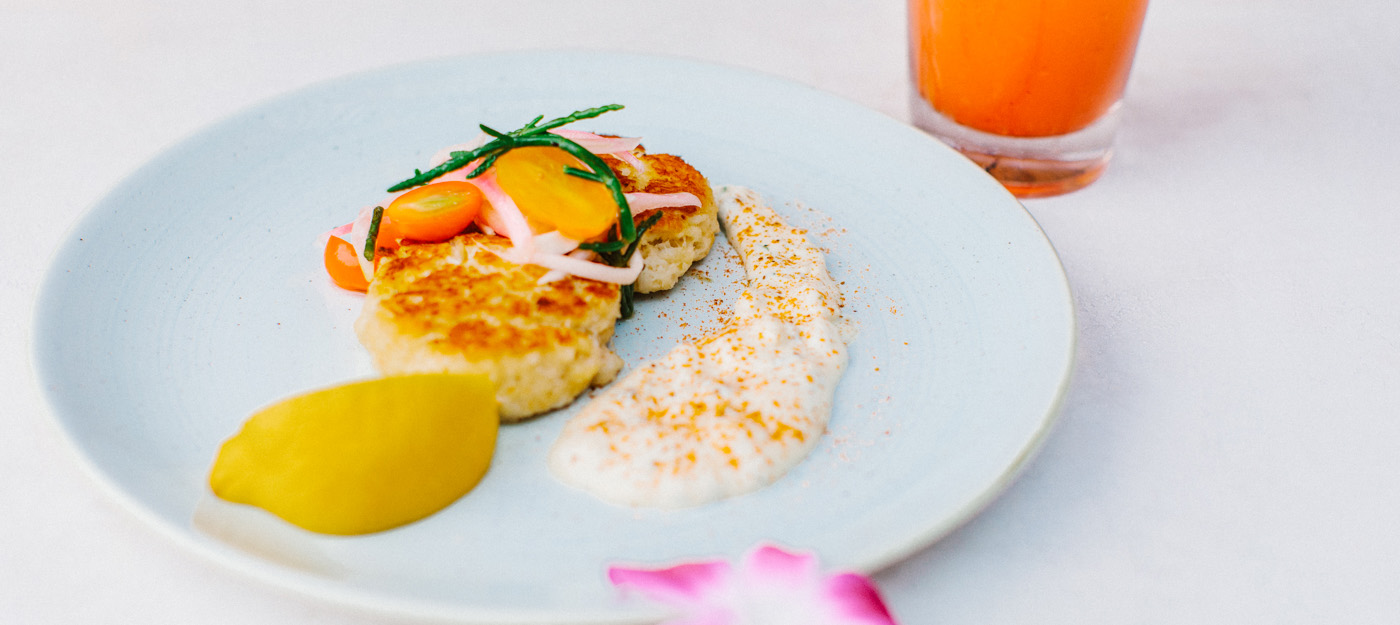 Crab cakes garnished with tomatoes and onions and a dipping sauce