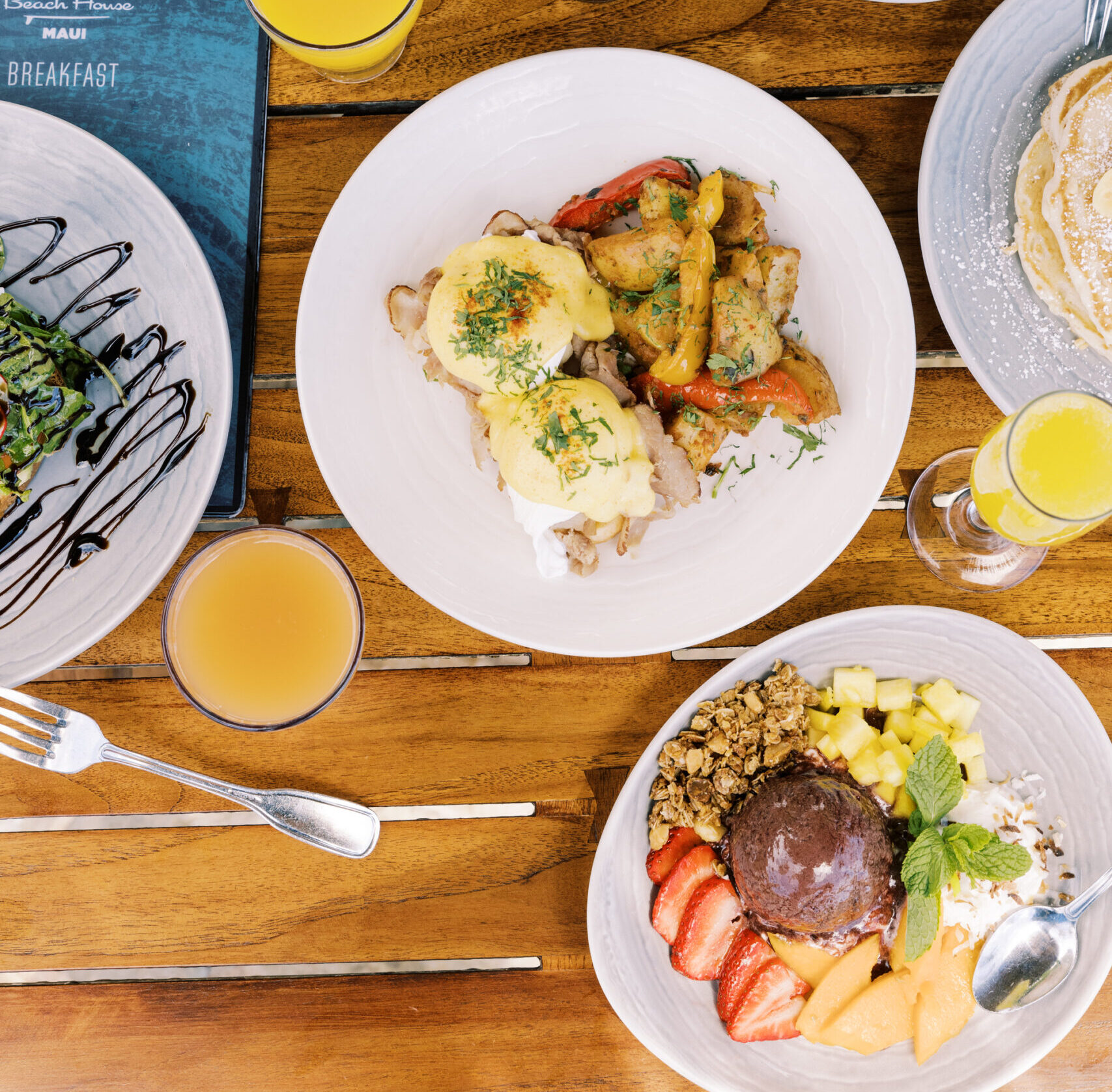 top down view of egg benedict with acai bowl and breakfast cocktail