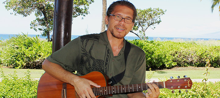 Keali’i Lum with guitar in front of sunny beach park